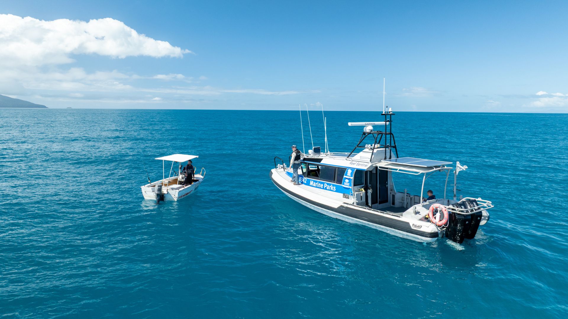 Two boats, one smaller and one larger float beside one another on the water.