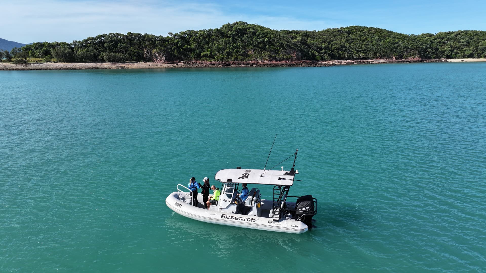 A research boat on the water with a vegetated shoreline in the background.