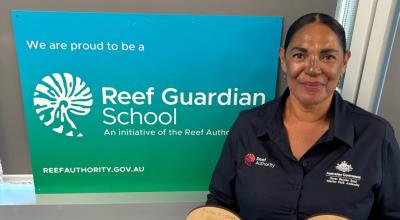 Marica Townsend stands in front of a Reef Guardian School sign in a corporate button up shirt.