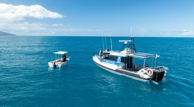 Two boats, one smaller and one larger float beside one another on the water.