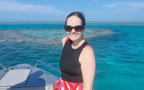 Woman poses on a boat before a reef with blue waters.