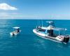 Two boats, one smaller and one larger float beside one another on the water.